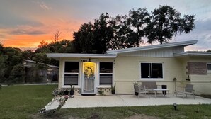 Uma casa térrea com varanda frontal, placa com o número 5445 e um pequeno pátio com mobiliário de exterior.