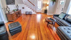 A spacious living room with hardwood flooring, a staircase, a black leather sofa, a wooden cabinet, and a television mounted on the wall. - Blueberry Cottage - Downtown Park City (Park City)