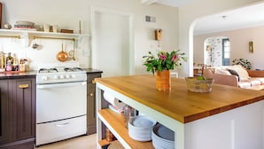 Una cocina con estufa blanca, encimera de madera y repisas con utensilios de cocina.