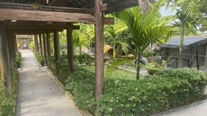 Un paseo techado con columnas de madera, rodeado de abundante vegetación y plantas.