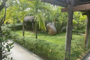 A garden with a thatched-roof structure, a large rock, and a wooden pergola. - Citrus Village Villa Hoi An (Hoi An)