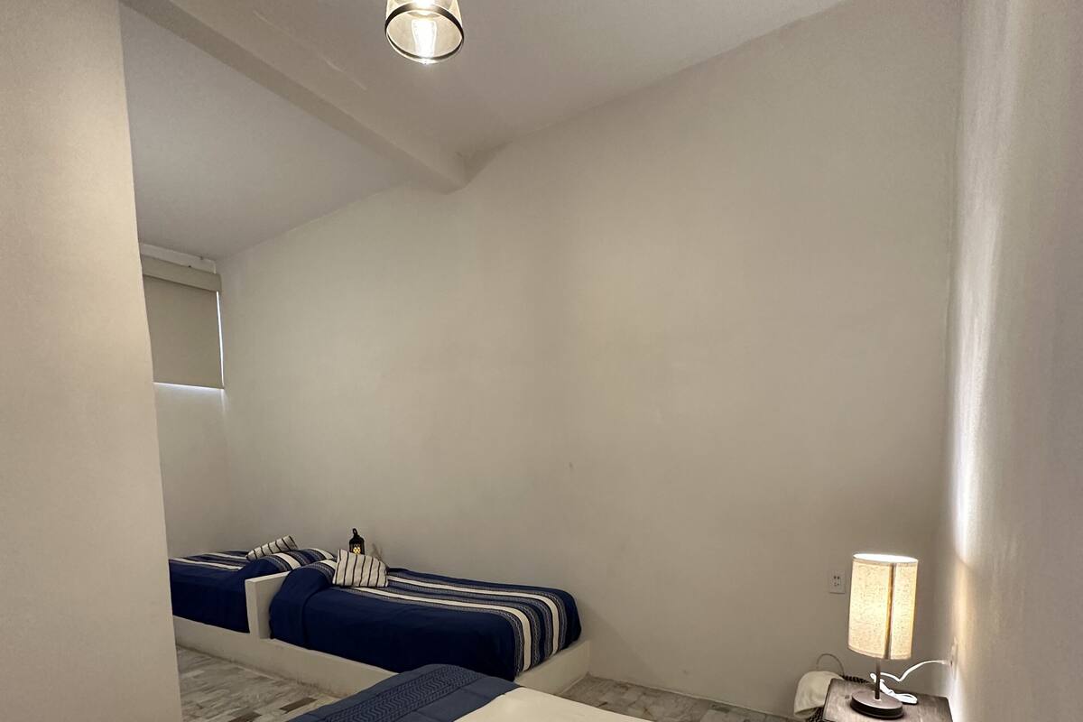 Un dormitorio con dos camas, una lámpara colgante, una mesita de noche con lámpara y un espejo en la pared.