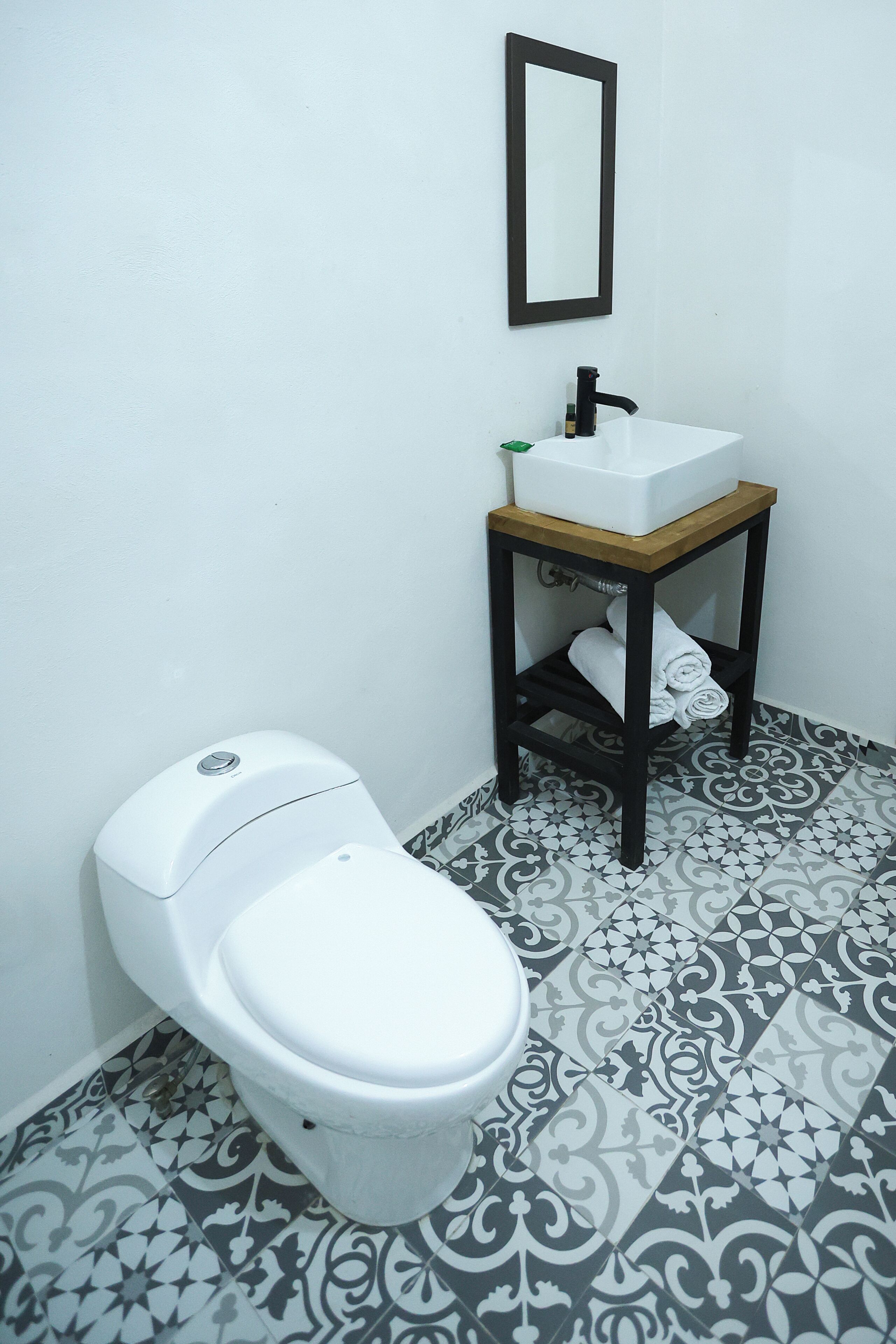Un baño con inodoro, lavabo sobre un pedestal de madera y baldosas de suelo estampadas.