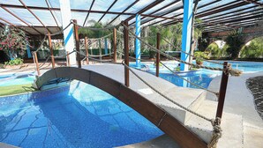 Una piscina con un puente de cristal, rodeada por una zona cubierta con cuerdas y columnas.