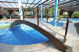 A swimming pool with a glass bridge, surrounded by a covered area with ropes and columns.