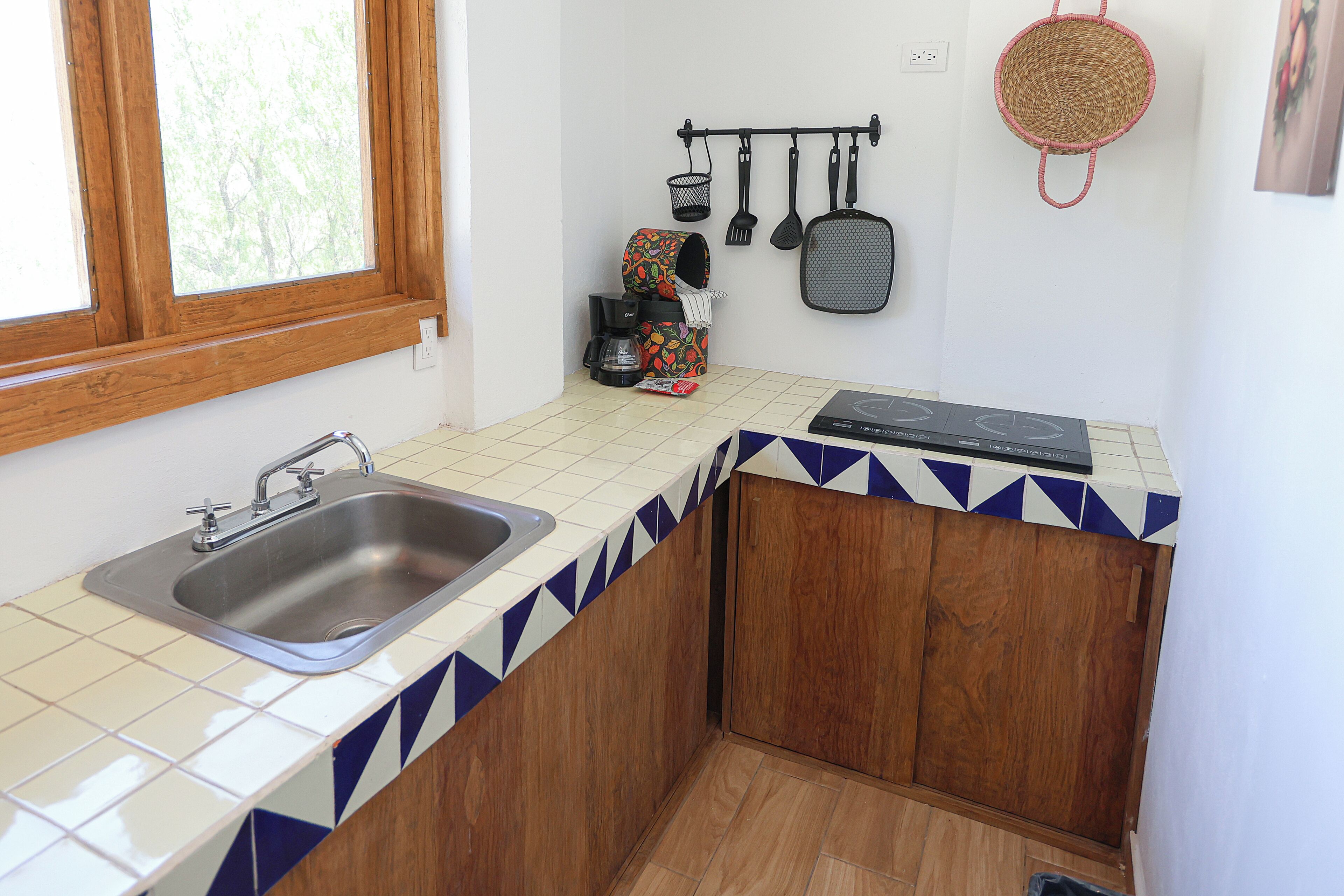 A small kitchen with a sink, wooden cabinets, a window, and a tiled backsplash.