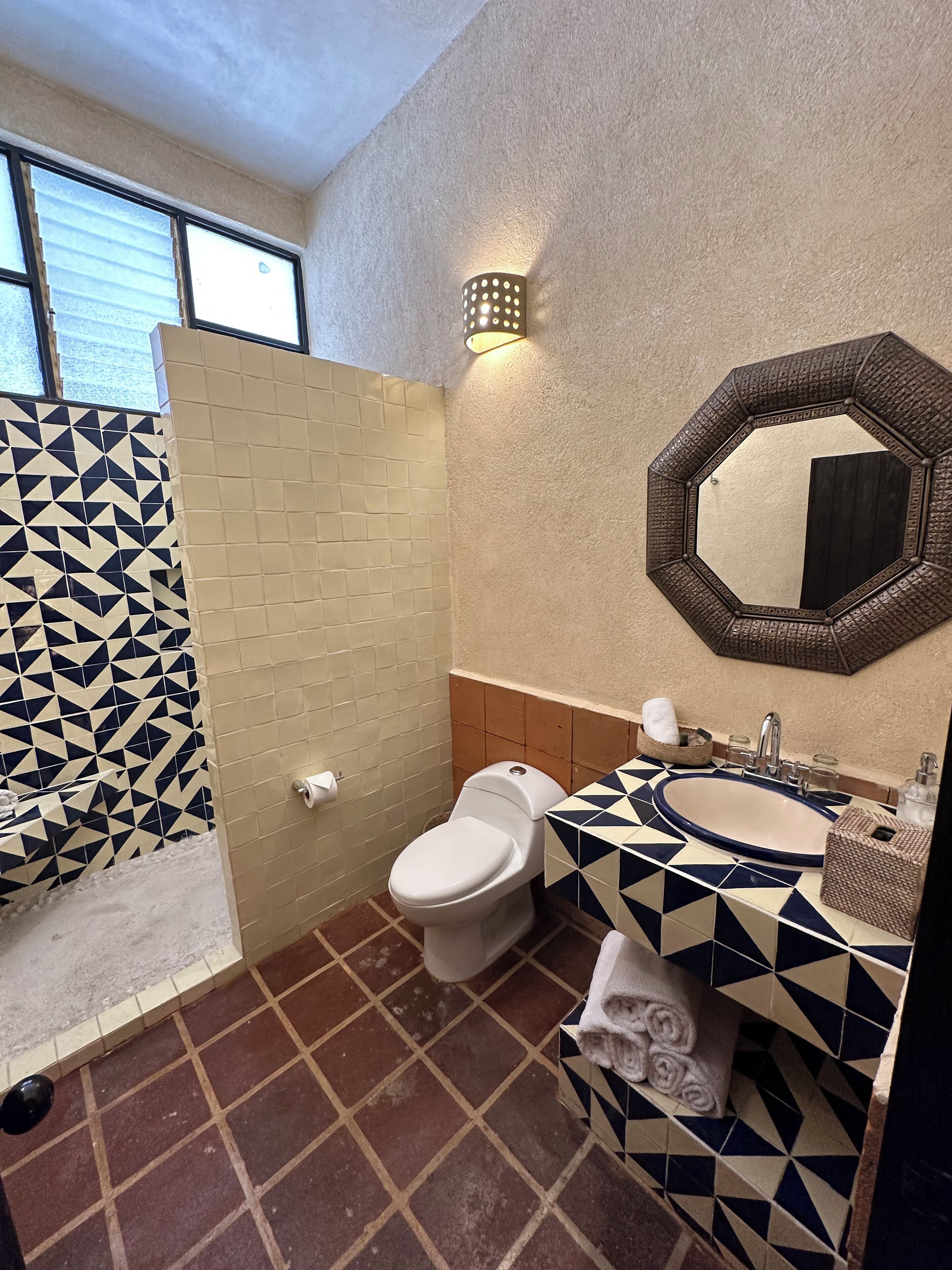 Un baño con un salpicadero de azulejos de diseño geométrico, un inodoro blanco, un lavabo con espejo y un perchero para toallas.