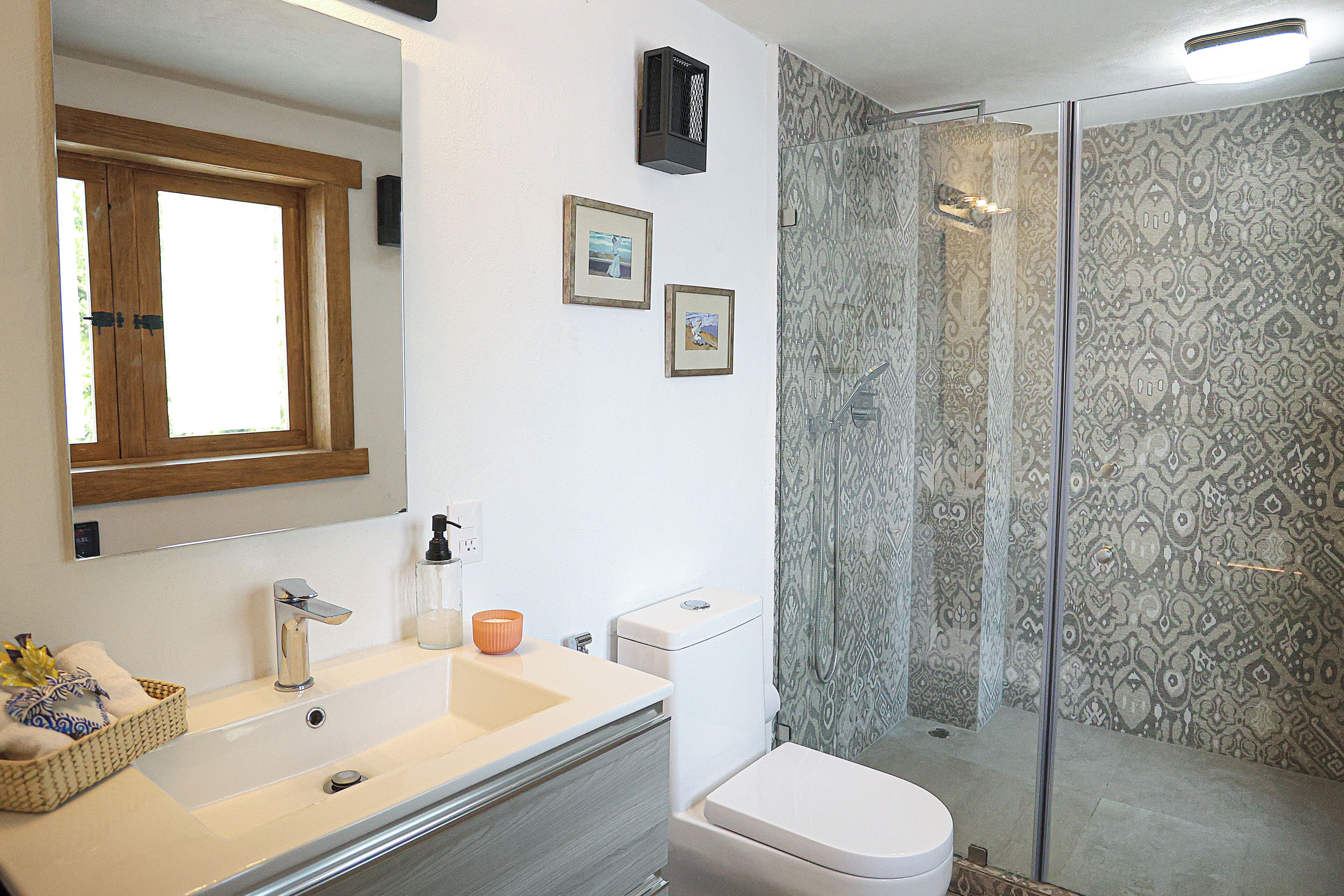 Een badkamer met een spiegel met houten lijst, een witte wastafel met chromen kraan, een wit toilet en douchegordijnen met een patroon.