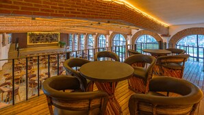 Un restaurante con paredes de ladrillo, ventanas de arco y suelo de madera. Mesas y sillas dispuestas para comer.
