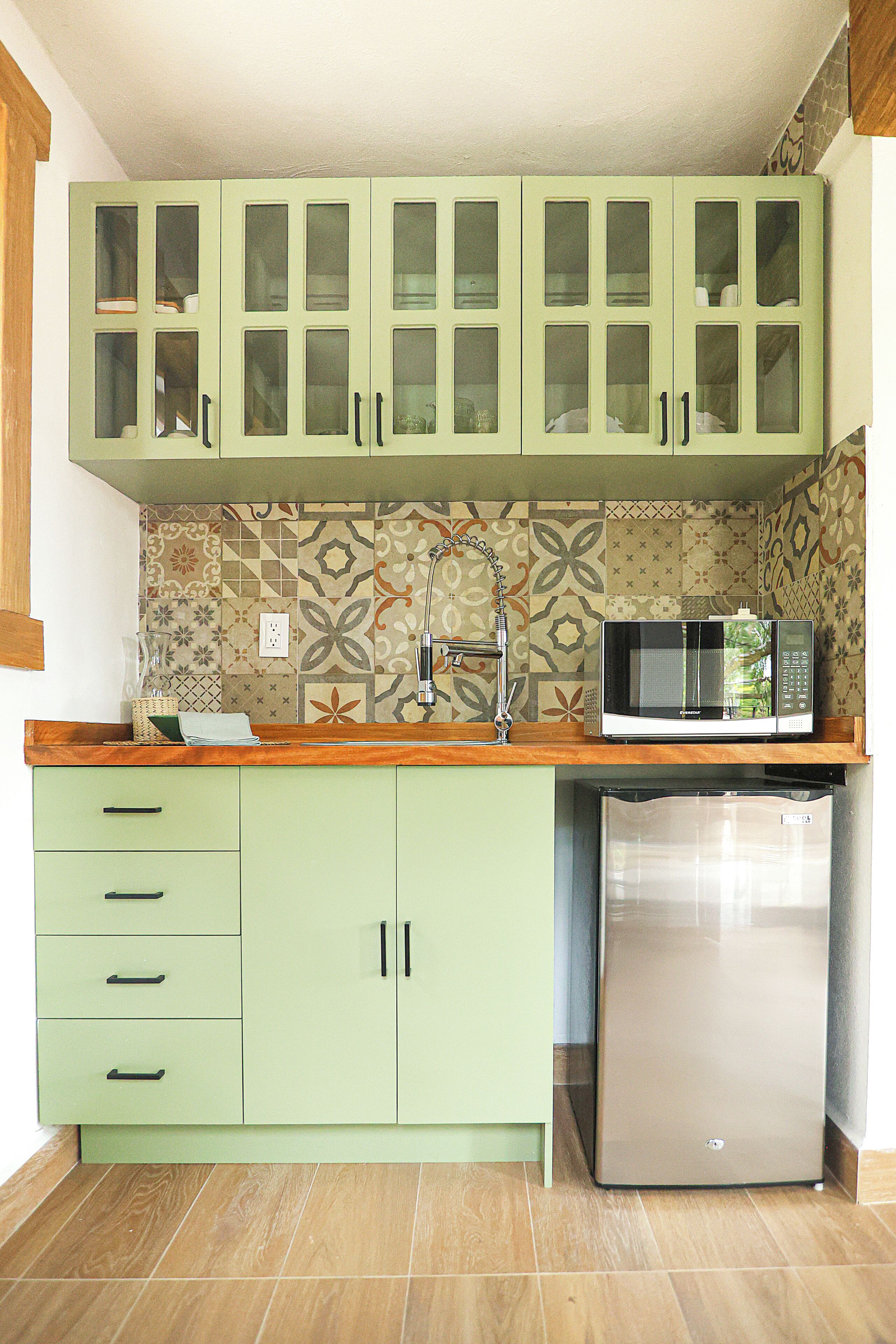 A kitchen with green cabinets, a microwave, and a stainless steel refrigerator.