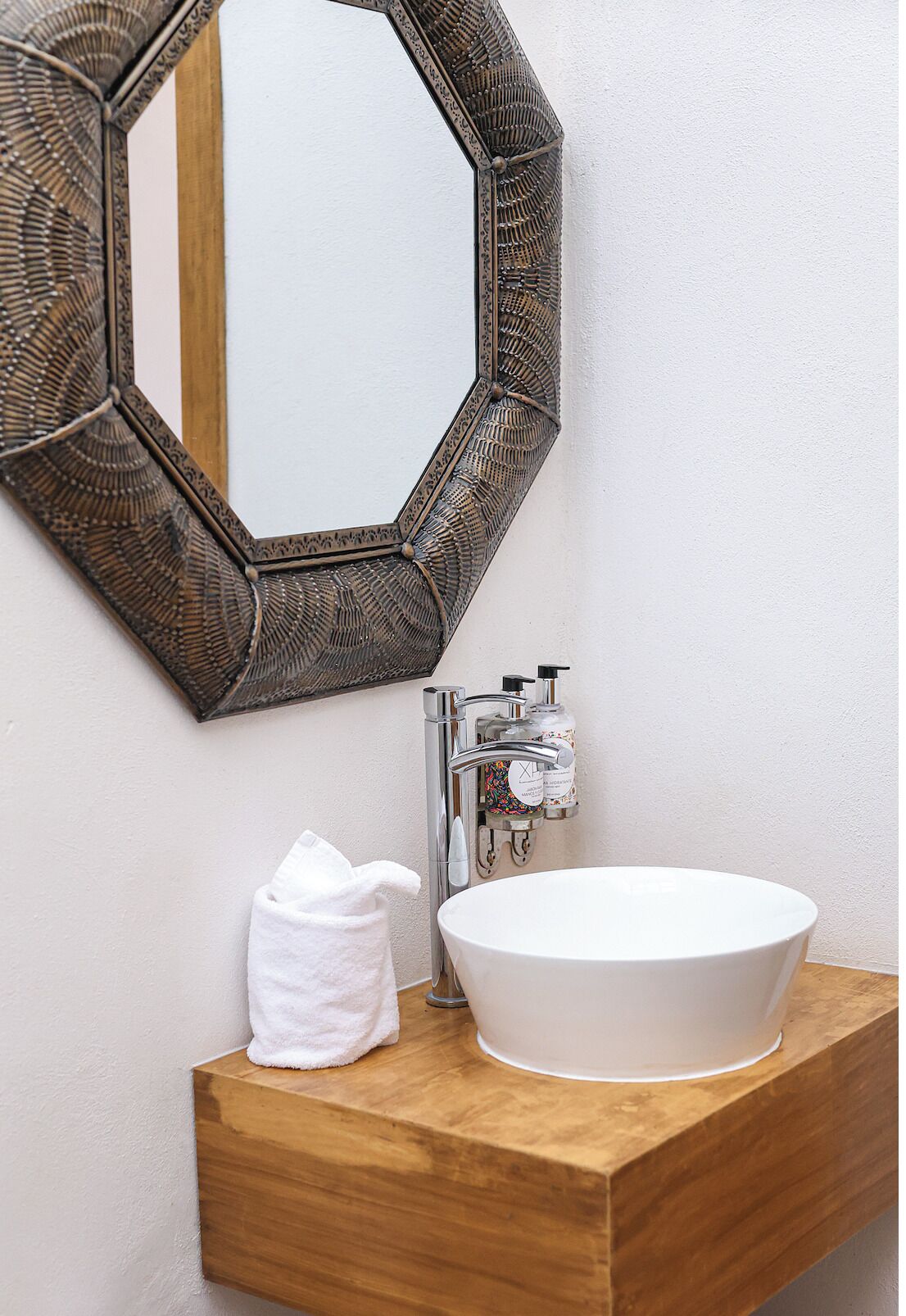 A bathroom with a wooden vanity, a white sink, a mirror with a decorative frame, and a towel on the counter.