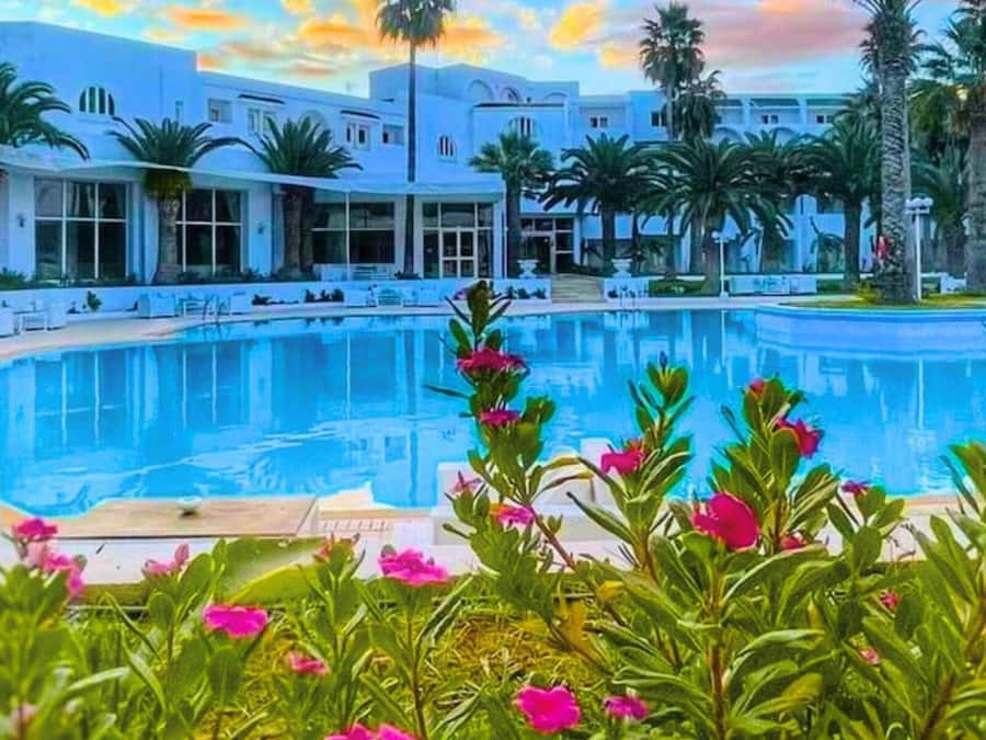 A pool surrounded by palm trees and a building with large windows.