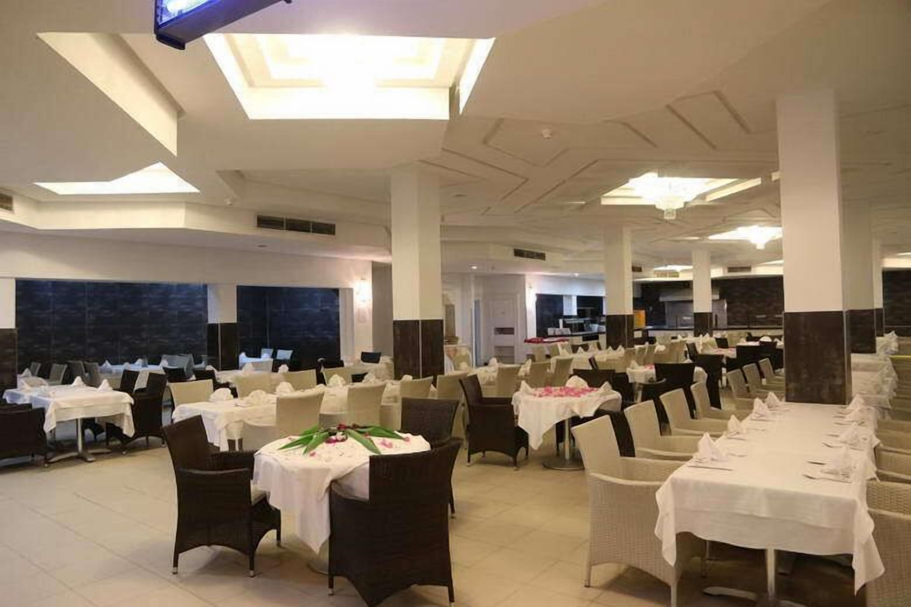 Une vaste salle de banquet avec de nombreuses tables dressées pour le repas, de hauts plafonds dotés de verrières et une architecture moderne.