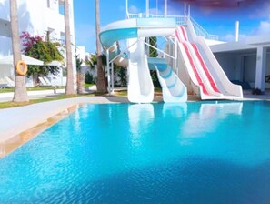 Una piscina con diversi scivoli, un edificio bianco e palme sullo sfondo.