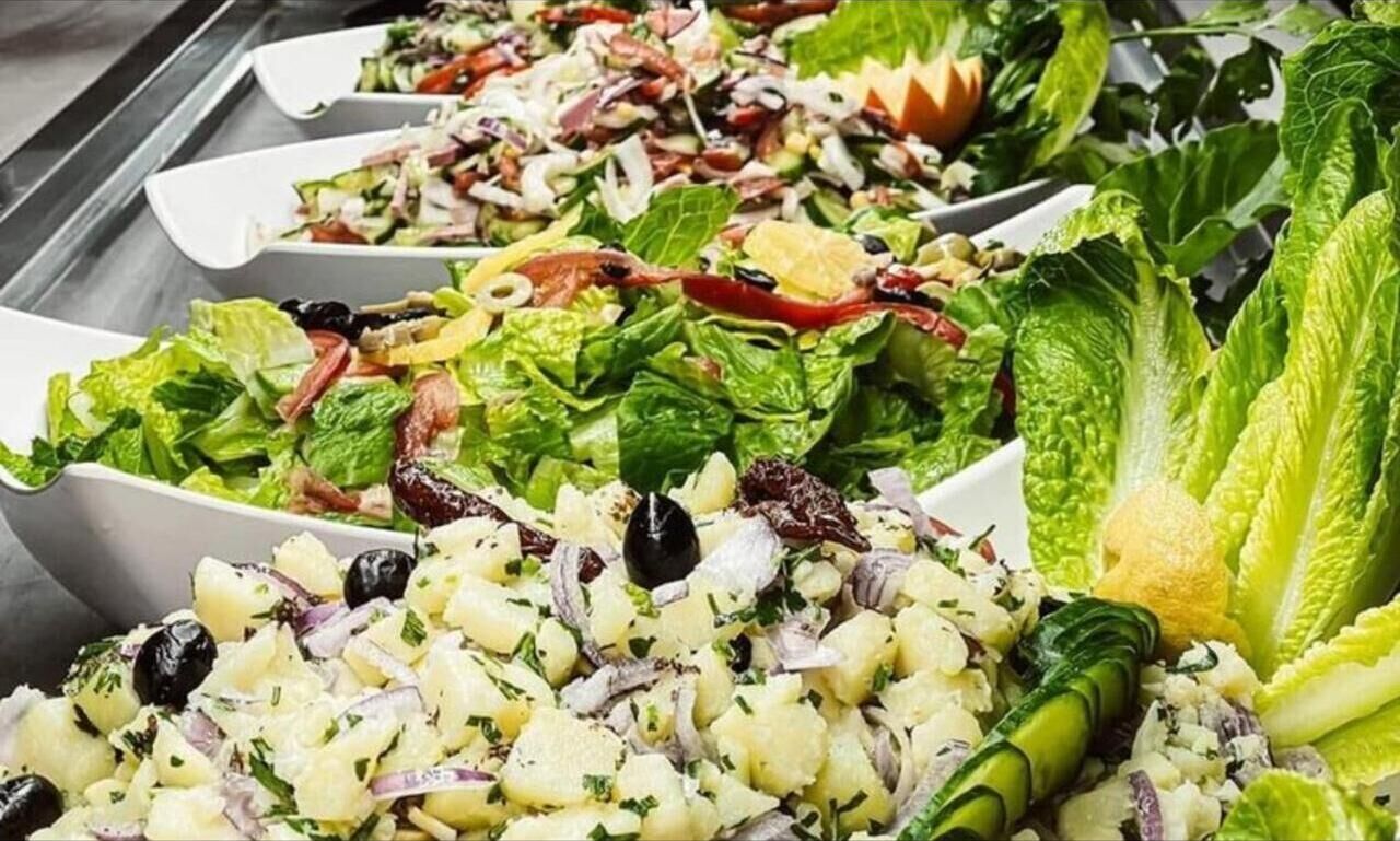 A buffet with various salads, including a Caesar salad, a potato salad, and a mixed greens salad.
