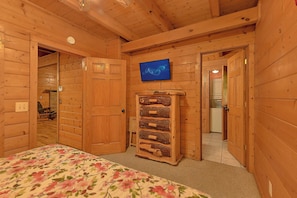 A wooden cabin interior with a bed, a television mounted on the wall, and a wooden cabinet. - Smoky Haven Hideaway in Gatlinburg (Gatlinburg)