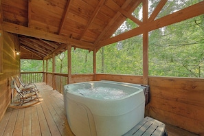 A wooden deck with a hot tub, rocking chairs, and a view of the forest. - Smoky Haven Hideaway in Gatlinburg (Gatlinburg)