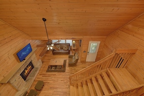A wooden cabin interior with a fireplace, a television, a sofa, a coffee table, and a staircase. - Smoky Haven Hideaway in Gatlinburg (Gatlinburg)