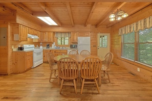 A wooden cabin-style kitchen with a dining table and chairs, a stove, microwave, refrigerator, and large windows. - Smoky Haven Hideaway in Gatlinburg (Gatlinburg)