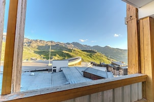 Vista desde un balcón con baranda de madera, con vistas a un paisaje montañoso y un edificio moderno de techo curvo.