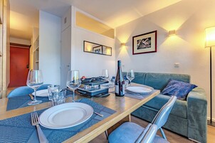 Un coin repas avec une table en bois dressée pour deux personnes, deux chaises et un canapé vert en arrière-plan.