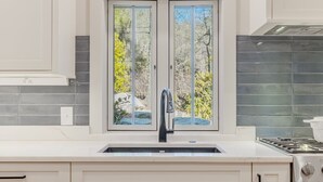 Een moderne keuken met een groot raam, witte kasten en een roestvrijstalen afzuigkap.