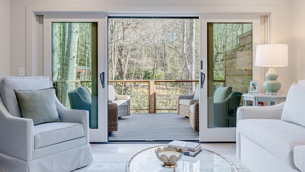 Een moderne woonkamer met een glazen deur die uitkomt op een terras met buitenmeubels.