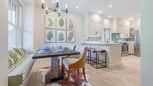 Een moderne keuken met witte kasten, een centraal eiland en een eethoek met een tafel en stoelen.