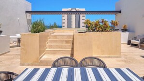 A rooftop terrace with a dining area, a set of stairs, and a view of a building in the background. - Apratamento Salinas Emerald - Yucatan Home Rentals (Progreso)