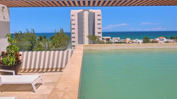 A rooftop pool with a view of the ocean and a tall building in the background. - Apratamento Salinas Emerald - Yucatan Home Rentals (Progreso)