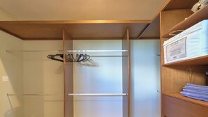 A walk-in closet with a wooden door, a hanging rack, and a shelf with folded towels. - Apratamento Salinas Emerald - Yucatan Home Rentals (Progreso)