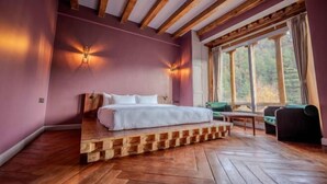 Une chambre à coucher avec un lit, des poutres en bois, une fenêtre avec des rideaux et une vue sur les arbres.