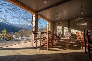 A room with wooden flooring, stone walls, and a large window overlooking a mountainous landscape.