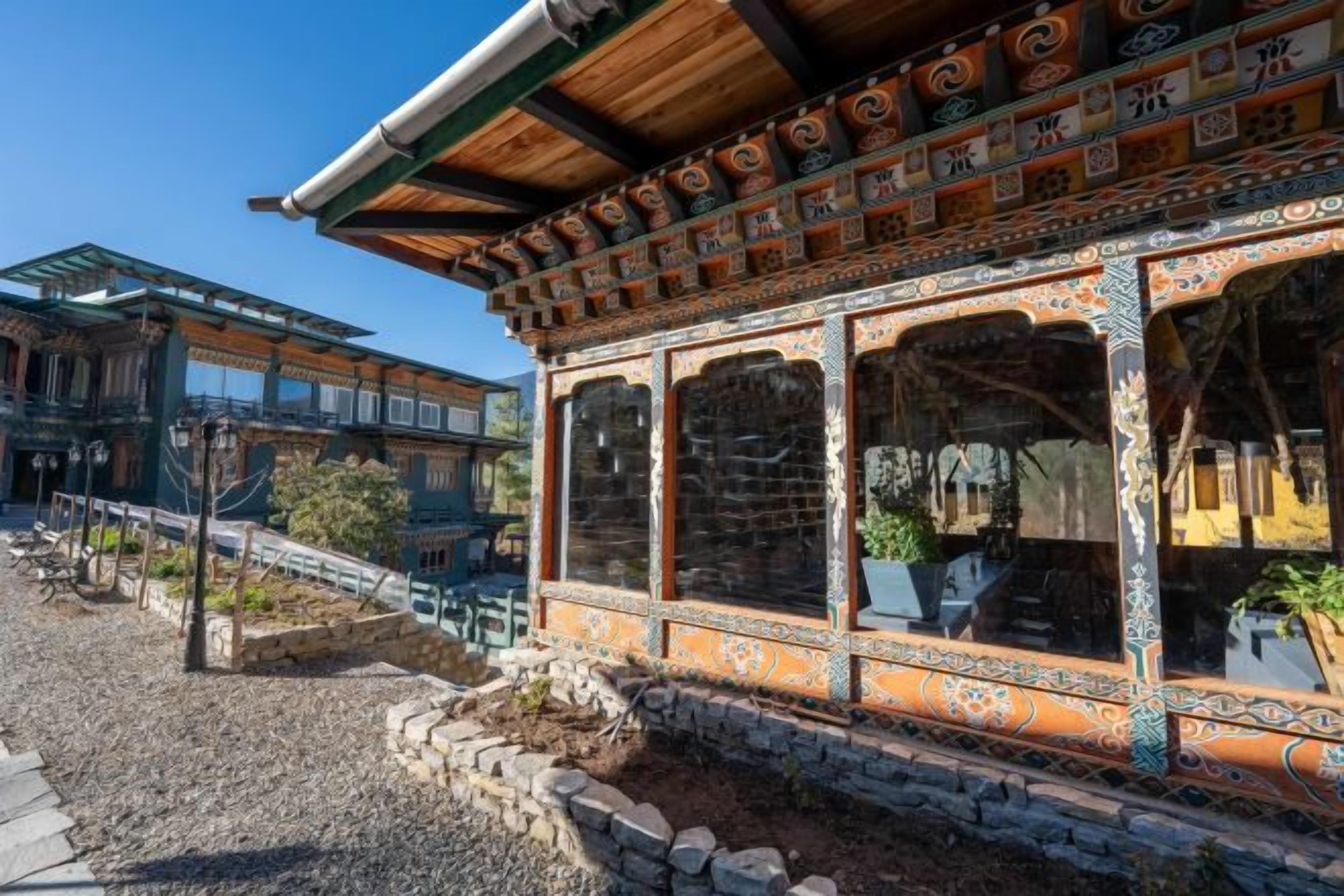 A traditional building with ornate wooden and stone architecture, large windows, and a stone pathway leading to a bridge.