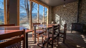 Un espace repas avec des tables et des chaises en bois, de grandes fenêtres et un mur en pierre.