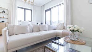 Ein modernes Wohnzimmer mit einem beigefarbenen Sofa, einem Glastisch und einer Vase mit weißen Blumen.