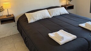 A double bed with a black bedspread, two white pillows, and two white towels folded on the bed. There are two bedside tables with lamps and a small shelf with a vase of flowers. Three framed pictures are hung on the wall above the bed. - Perfect 3-bedroom house in Santa Rosa de Calamuchita (Santa Rosa de Calamuchita)