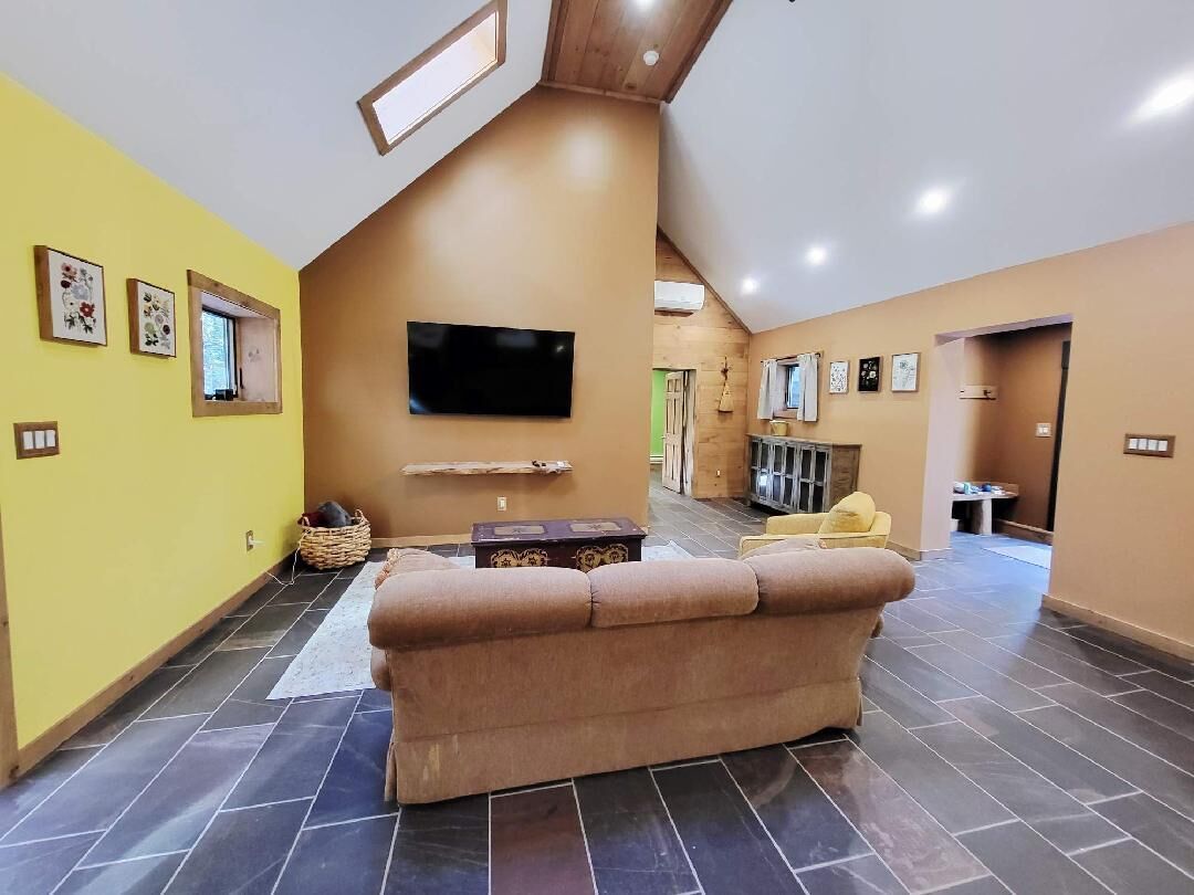 Un vaste espace de vie doté d’un haut plafond, d’un téléviseur à écran plat fixé au mur, d’un canapé beige et d’un fauteuil jaune.
