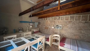 A rustic room with a stone wall, wooden beams, a glass table, and a bed with patterned bedding. - Romantic Stone House and Yard Near Stunning Beach (Trogir)