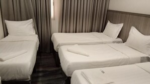 Quarto de hotel com três camas de solteiro dispostas em linha, cabeceira de madeira e uma janela com cortinas.