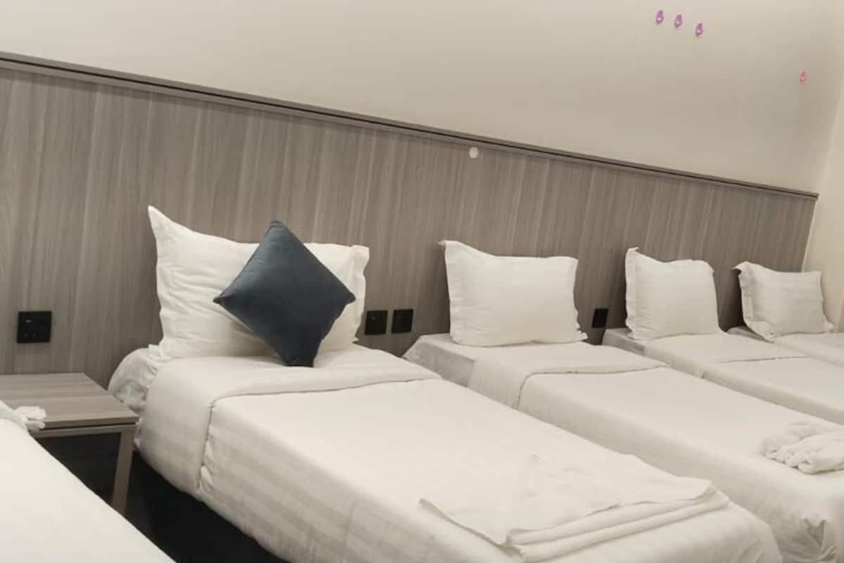 A hotel room with four single beds, each with white bedding and a pillow.