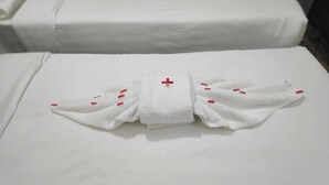 Toalha branca dobrada com listras vermelhas sobre uma cama.
