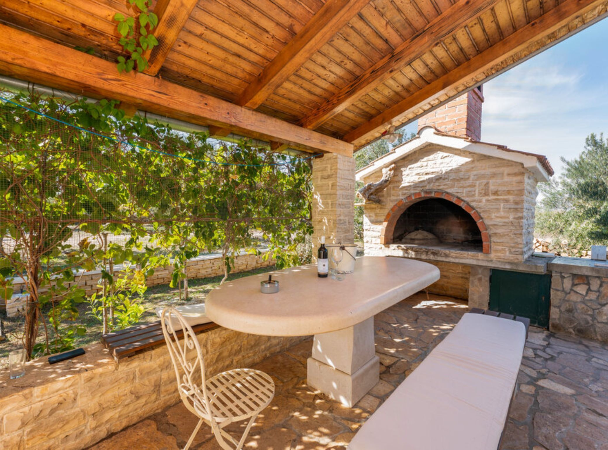 An outdoor patio with a stone table, a chair, and a brick oven.