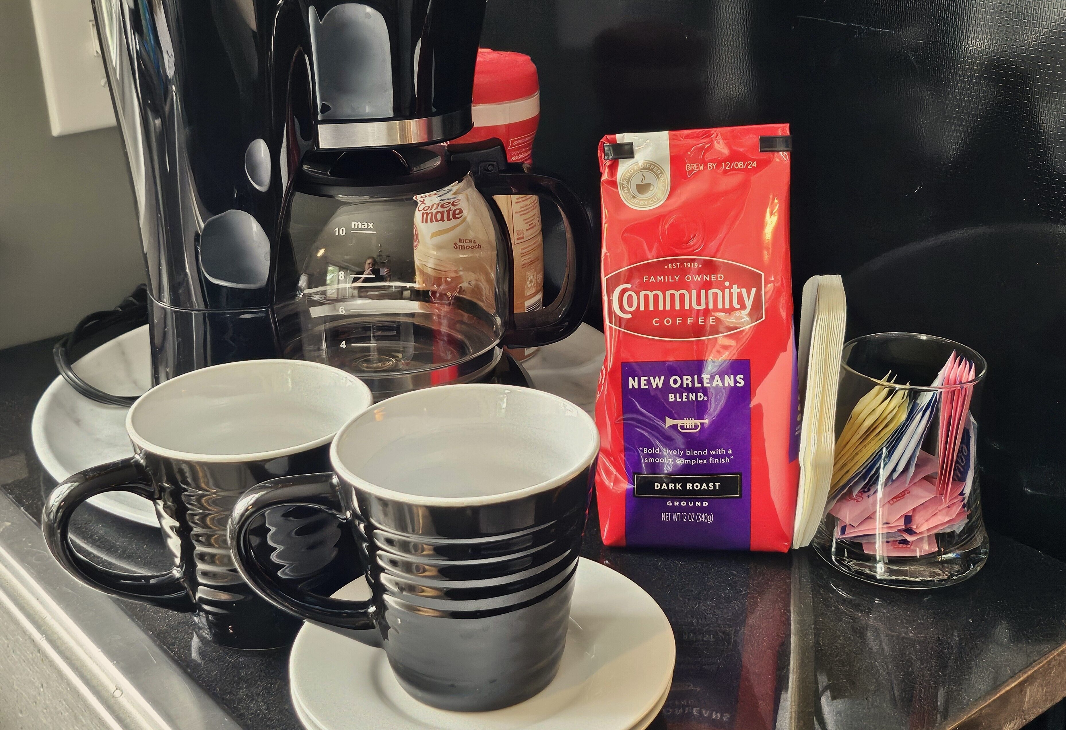 Eine Kaffeemaschine, eine Kaffeepackung und mehrere Tassen auf einer Arbeitsplatte.