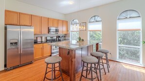 A modern kitchen with wooden cabinets, stainless steel appliances, a central island with stools, and large windows with views of greenery. - Stylish Houston Getaway (Houston)