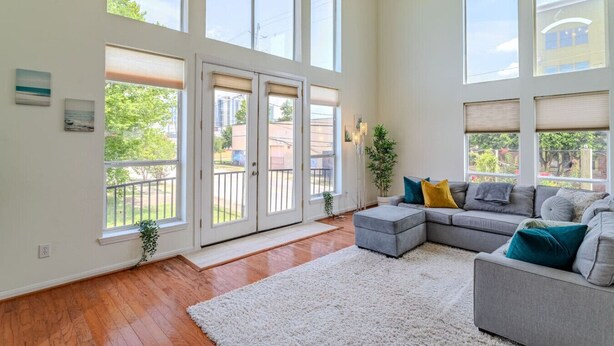 A spacious living room with a grey sectional sofa, a white shag rug, and large windows offering a view of the outdoors. - Stylish Houston Getaway (Houston)