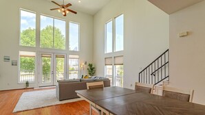 A spacious living room with a large wooden dining table, a gray sofa, and a staircase leading to an upper level. - Stylish Houston Getaway (Houston)