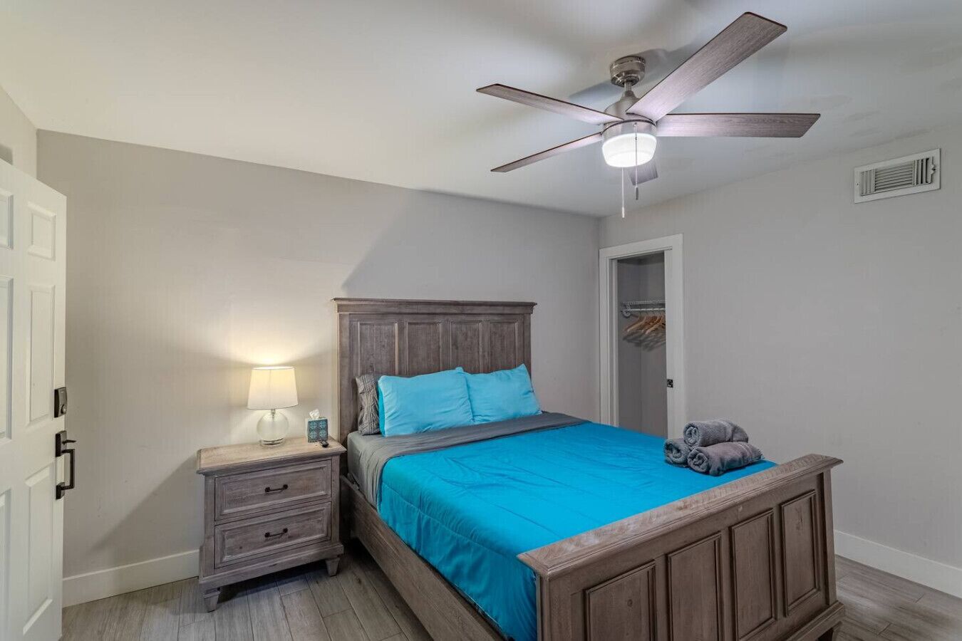 A bedroom with a wooden bed, a nightstand, a ceiling fan, and a door leading to a closet.