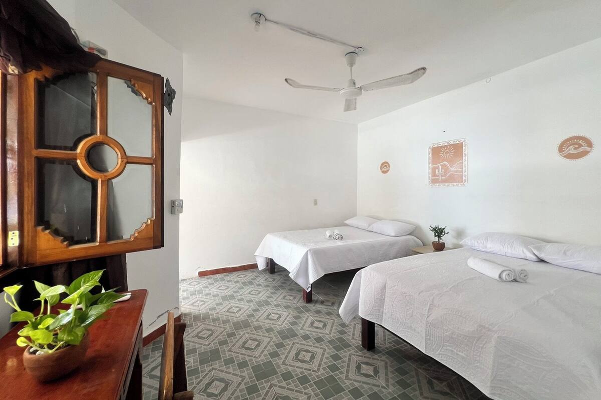 Quarto com duas camas, um ventilador de teto, um armário de madeira e piso estampado.