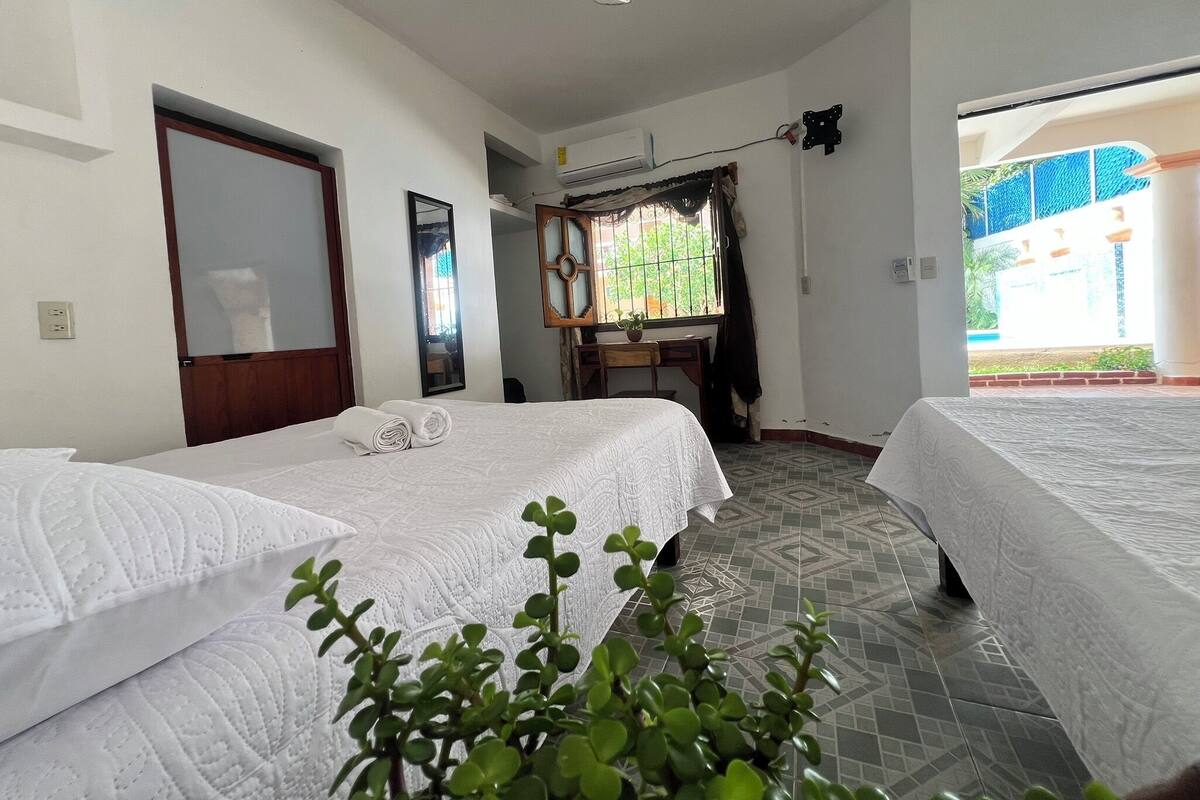 Quarto de hotel com duas camas, uma escrivaninha, um espelho e uma janela com vista para o exterior.